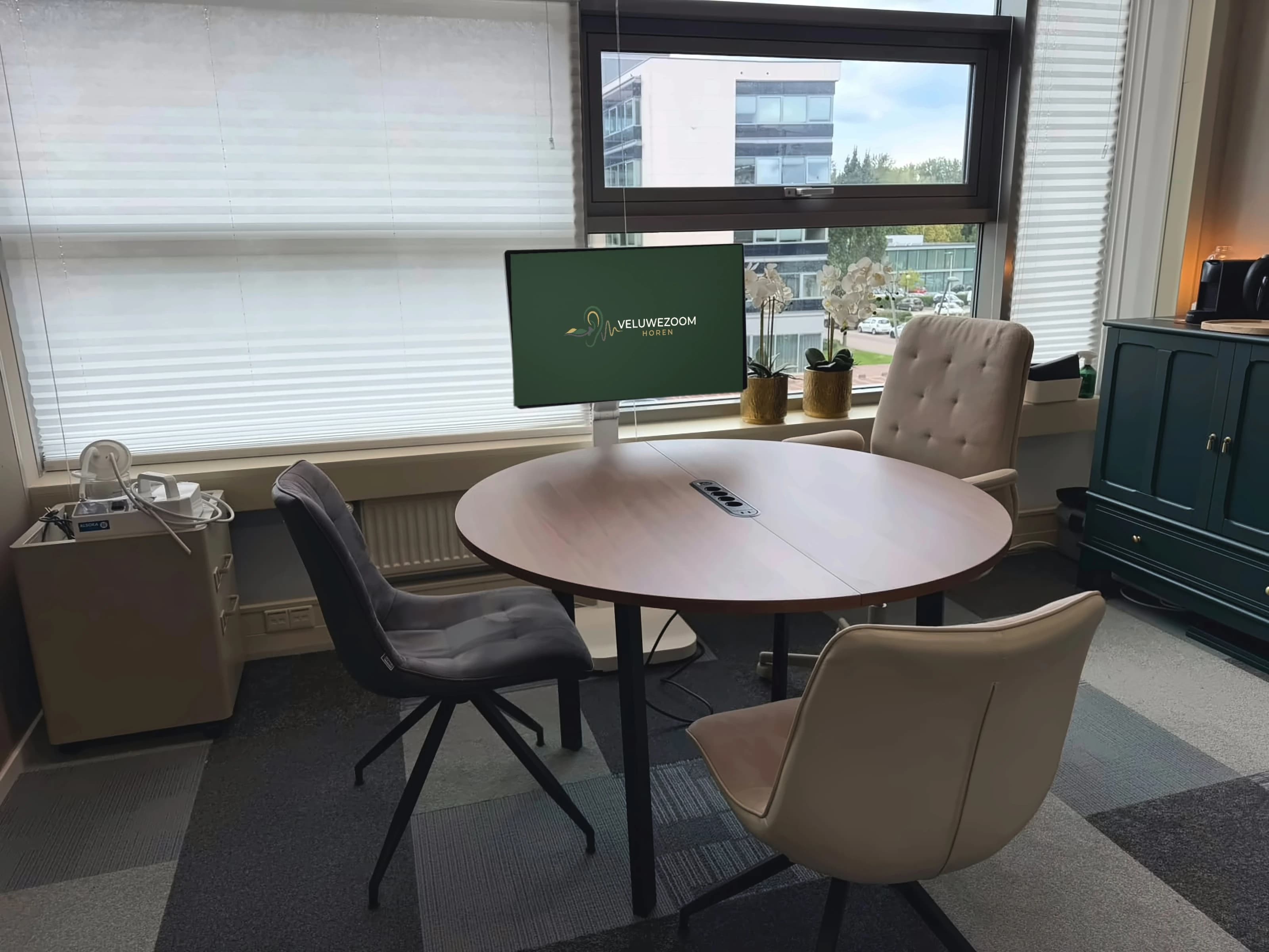 De praktijkruimte met een ronde overlegtafel bij het raam